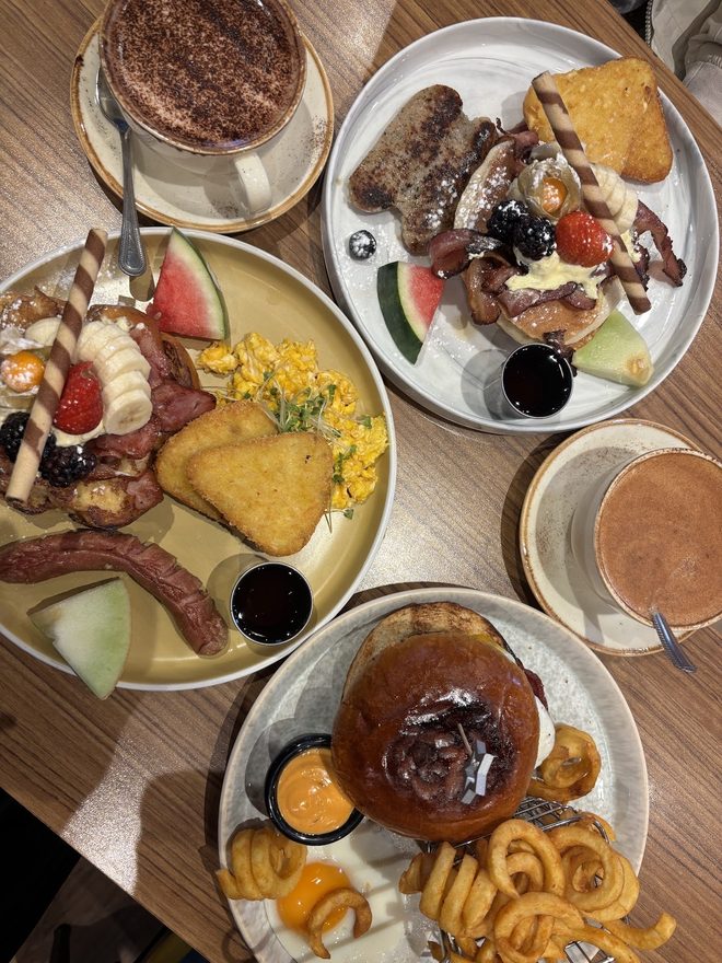 Table of brunch plates with pancake stacks, cooked breakfast and a burger