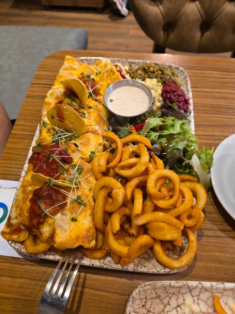 Cheese-topped flatbread on a board with curly fries and a sauce pot