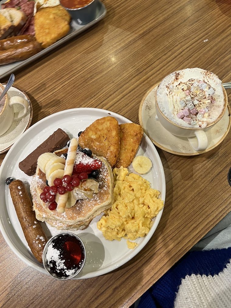 Pancakes and a cooked breakfast on the table with a loaded hot chocolate